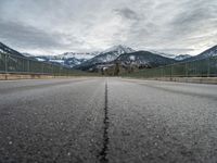 empty road with mountain in distance under cloudy sky and metal railings in foreground