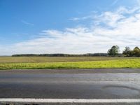 an empty road with grass and trees in the background on the horizon, with a blue sky above