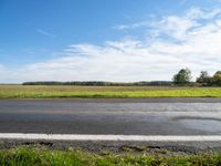 an empty road with grass and trees in the background on the horizon, with a blue sky above