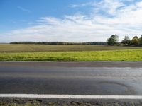 an empty road with grass and trees in the background on the horizon, with a blue sky above