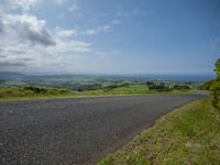 an empty road with green grass and hills in the background and some sky with clouds