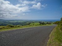 an empty road with green grass and hills in the background and some sky with clouds