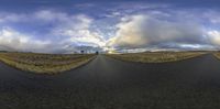 there is a large empty paved road with clouds in the sky above it and the ground below