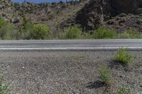 a fire hydrant sits on an empty road in front of a mountainous area with rocky hills and trees