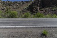 a fire hydrant sits on an empty road in front of a mountainous area with rocky hills and trees