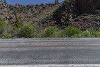 a fire hydrant sits on an empty road in front of a mountainous area with rocky hills and trees