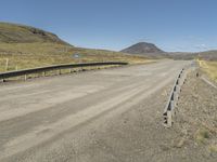 a road with no cars or vehicles on it going past the mountains and grass on the other side