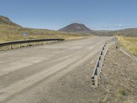 a road with no cars or vehicles on it going past the mountains and grass on the other side