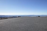 a long empty road with rocks and mountains in the distance in front of it and blue skies above