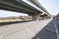 the empty road beside the roadway under an overpass of a highway bridge and soccer field