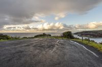 an empty road sits on the side of a hill with a view of the sea