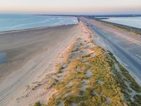 an aerial shot of an empty road that goes down to an ocean shore with a long, empty beach nearby