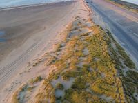 an aerial shot of an empty road that goes down to an ocean shore with a long, empty beach nearby