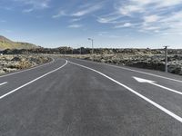 a empty road leading into the distance with a green mountain in the background is a cloudless sky