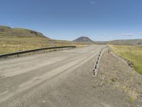 the empty road is near the grassy hills and mountains with signs on it along a mountain