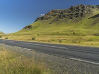 an empty road passing through the mountains with yellow flowers in a grassy field, on a clear day