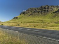 an empty road passing through the mountains with yellow flowers in a grassy field, on a clear day