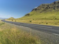 an empty road passing through the mountains with yellow flowers in a grassy field, on a clear day