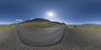 a view of an empty road with mountains and a cloudy sky above it with a fish eye lens