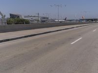 an empty road on a sunny day with cars driving in the background and an airport in the distance