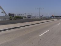 an empty road on a sunny day with cars driving in the background and an airport in the distance
