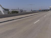 an empty road on a sunny day with cars driving in the background and an airport in the distance