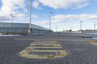 yellow paint marking the way to an empty road in a parking lot in an industrial area of city with white clouds and blue sky above