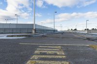 yellow paint marking the way to an empty road in a parking lot in an industrial area of city with white clouds and blue sky above