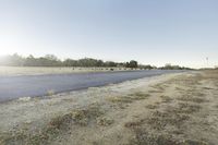an empty road with an intersection at the bottom, and some cows grazing in a field behind it