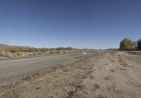 an empty road with an intersection at the bottom, and some cows grazing in a field behind it