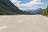 the road is empty on both sides and on the other side there is a lake and mountain range on both sides