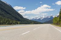 the road is empty on both sides and on the other side there is a lake and mountain range on both sides