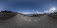 a fish eye view of a very empty road near a lake and some mountains and hills