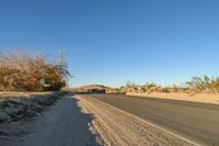 a empty street in the middle of a barren plain with dry grass growing beside it