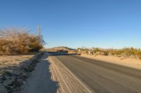 a empty street in the middle of a barren plain with dry grass growing beside it