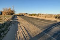 a empty street in the middle of a barren plain with dry grass growing beside it