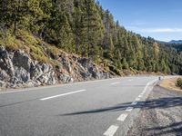 motorcycle riders are riding on an empty road with trees around them on both sides and a mountain in the background