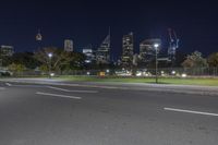 an empty road next to a large city at night with a green sign near the end