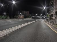 an empty road with lights on at night, by a brick building and parking lot