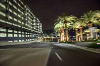 an empty highway with palm trees and tall buildings on both sides at night in the city