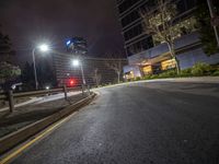 a red stoplight is next to some buildings and street lights at night time on an empty road