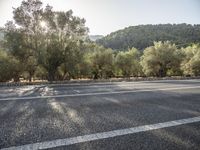 the empty road is lined with trees and mountains in the background there are lots of trees and hills