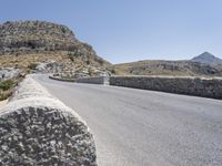 an empty road winding up to the peak of mountains with stone barriers in front of them