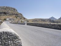 an empty road winding up to the peak of mountains with stone barriers in front of them