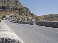 an empty road winding up to the peak of mountains with stone barriers in front of them