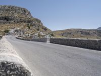 an empty road winding up to the peak of mountains with stone barriers in front of them