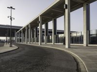 an empty road leading to a large open area with lots of columns and benches nearby