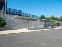 the empty road has a wooden structure beside it with metal barriers around it and a black iron fence surrounding