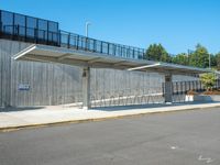 the empty road has a wooden structure beside it with metal barriers around it and a black iron fence surrounding