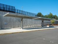 the empty road has a wooden structure beside it with metal barriers around it and a black iron fence surrounding